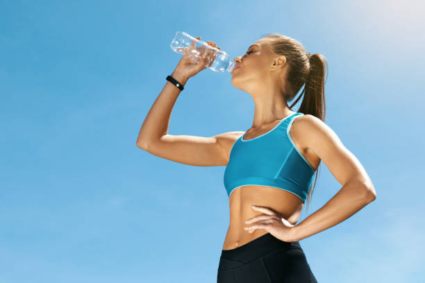 Woman Drinking Water After Running. Woman Drinking Water After Running. Portrait Of Beautiful Athletic Girl In Bright Colorful Sportswear Resting After Fitness Workout, Drink Water From Bottle On Blue Sky Background. High Quality Image hot women working out pictures stock pictures, royalty-free photos & images
