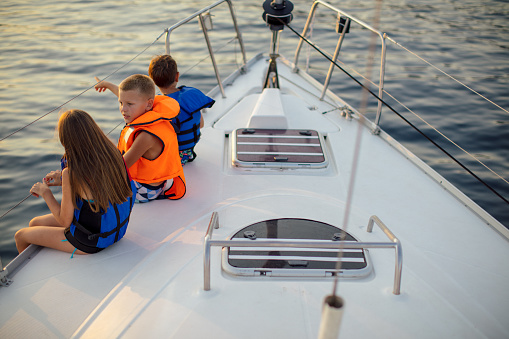 Children sitting on the sailboat deck with legs out of boat and enjoying at sunset and looking at distance