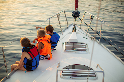 Children sitting on the sailboat deck with legs out of boat and enjoying at sunset and looking at distance