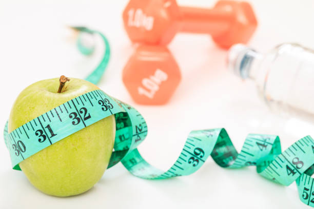 istock Green apple, dumbbells and measuring tape on white background 959609706