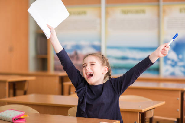 happy child sits at the desk in the classroom and enjoys the beginning of school holidays - mirth imagens e fotografias de stock