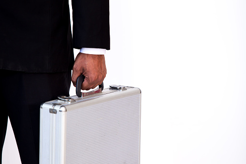 Business man in black suit carrying a hard suitcase isolated.