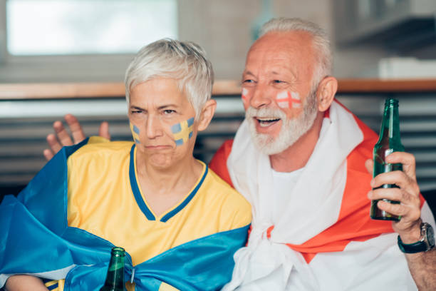 istock Swedish soccer enthusiast frowning and senior man supporting England cheering while watching the game 959634648