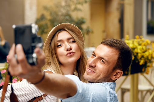 Beautiful Smiling Couple Having Fun Traveling, Taking Photos On Camera Outdoors On Street. Portrait Of Handsome Smiling Man And Happy Young Woman In Love Spending Time Together. High Quality Image.