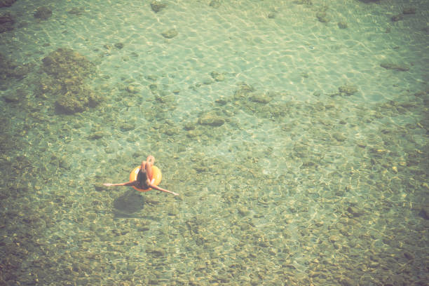 Young woman relaxing at the beach while sunbathing and floating on a mattress