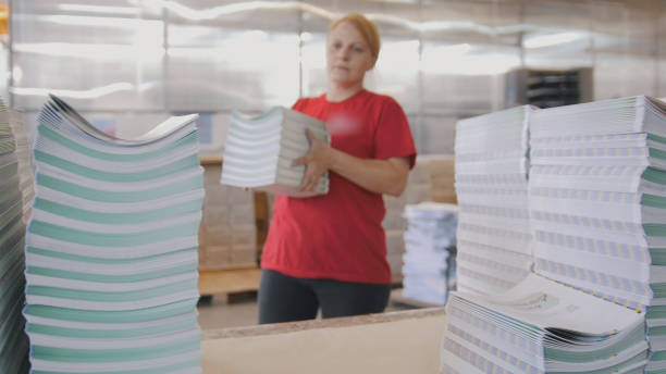 istock Female worker puts the printed magazines in stacks on the table in the typography 959641730