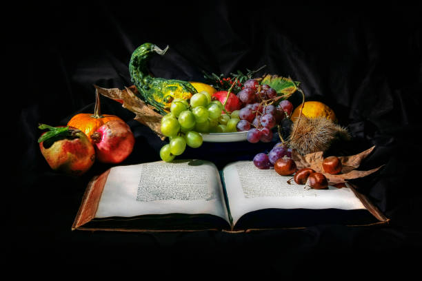 Still life with fresh fruit and chestnuts. Grapes, pomegranate and various types of pumpkin. Black background. Ancient book.