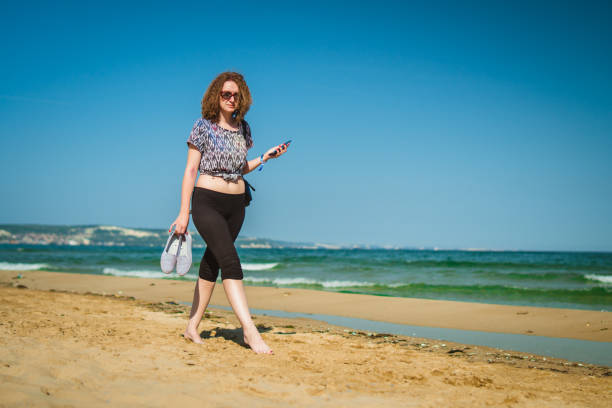 Young woman walking on sandy beach in beautiful sunny day.