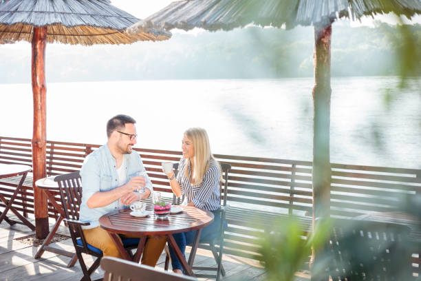istock Young couple drinking coffee and talking in a cafe by the river 959712652