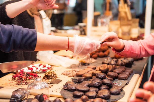 pantalla con surtido de dulces de chocolate oscuros y café con diferentes rellenos. mano del vendedor escoge alguna rodaja para el comprador prueba. sabrosos y deliciosos postres. enfoque selectivo. - tasting fotografías e imágenes de stock