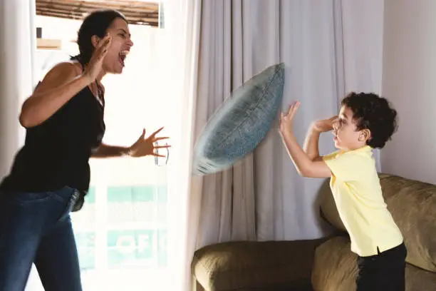 Mother and son playing pillow fight in the couch.