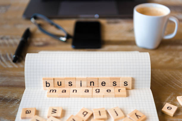 istock Closeup on notebook over wood table background, focus on wooden blocks with letters making Business Manager words 959720770