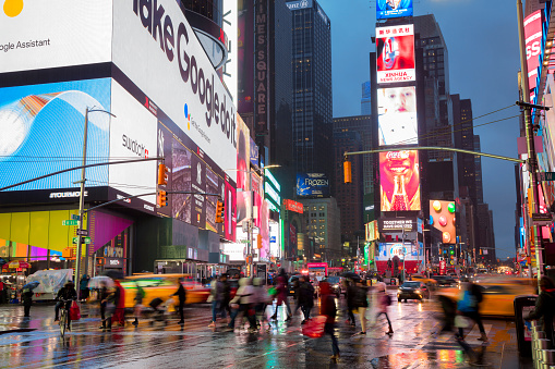 Pedestrians and tourist walking with umbrellas at dusk, rainy day at Times Square, advertising and billboard are visible in the background, Manhattan, New York, America, USA.