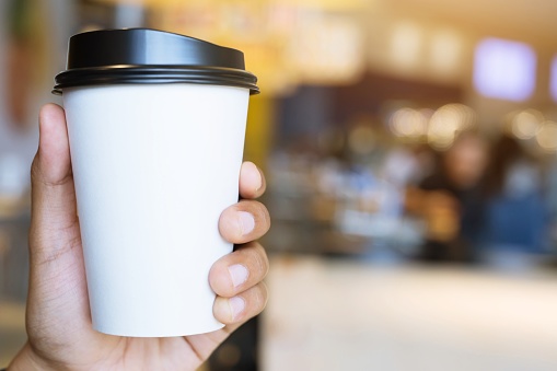 people hand holding paper cup of take away drinking coffee show on clear sky blue natural morning sunlight. space Place for your text or logo. empty space for text.