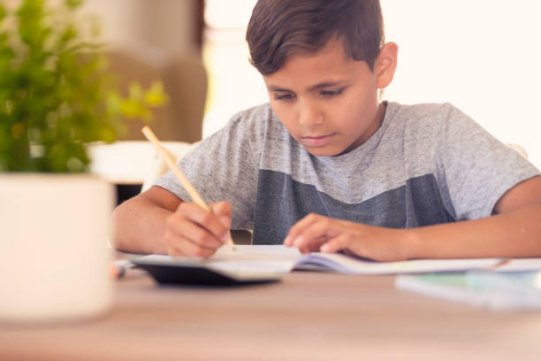 Young Aboriginal boy doing homework. Young Aboriginal boy doing homework. He is sitting at a table alone. He is concentrating on writing. He may be a little sad or worried sad african child drawings stock pictures, royalty-free photos & images