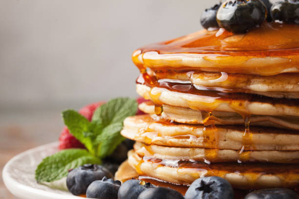 istock Close-up delicious pancakes, with fresh blueberries, strawberries and maple syrup on a light background. Sweet maple syrup flows from a stack of pancake 959761226