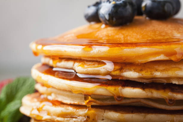 istock Close-up delicious pancakes, with fresh blueberries, strawberries and maple syrup on a light background. Sweet maple syrup flows from a stack of pancake 959761238