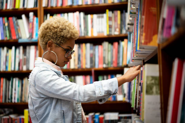 studente che sceglie un libro sulla biblioteca - library student latin american and hispanic ethnicity university foto e immagini stock