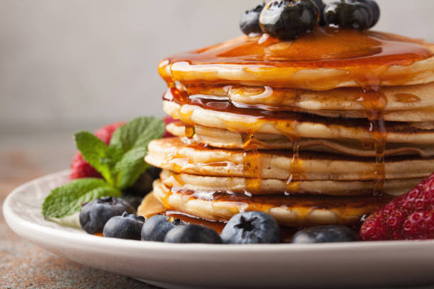 istock Close-up delicious pancakes, with fresh blueberries, strawberries and maple syrup on a light background. Sweet maple syrup flows from a stack of pancake 959761336