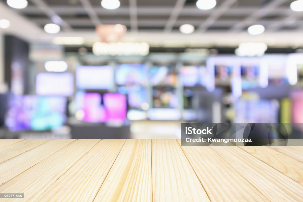 wood table top with eletronic department store show Television TV and home appliance with bokeh light blurred background Advice Stock Photo