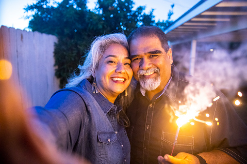 A senior mexican couple holds a sparkler while taking a selfie at a party