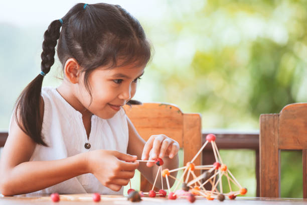 Cute asian child girl playing and creating with play dough and toothpick Cute asian child girl playing and creating with play dough and toothpick. Child concentrated with play dough building a molecule model. toothpick stock pictures, royalty-free photos & images