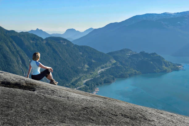 Person on granite cliff enjoying the scenic view of Sea-To-Sky road and ocean bay surrounded with mountains. Squamish. Whistler. Stawamus Chief Provincial Park. British Columbia. Canada. garibaldi park stock pictures, royalty-free photos & images