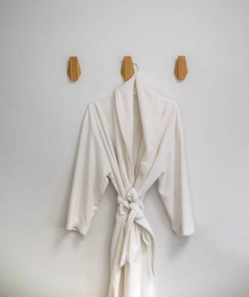 istock Classic bathrobe hanging on wooden abstract wall hook mounted against white wall 959788366