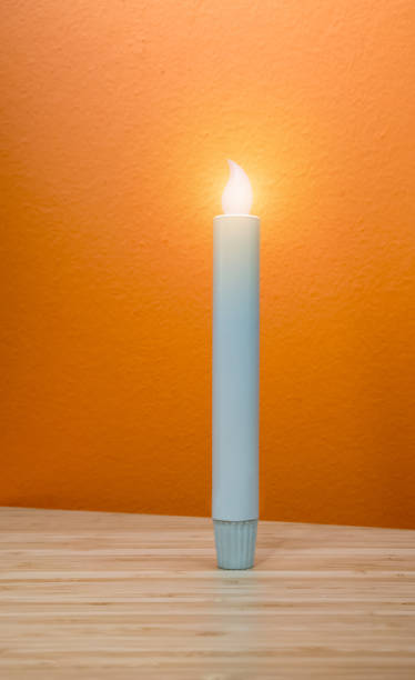 istock LED candle light standing on wooden table isolated against yellow orange background. 959791782