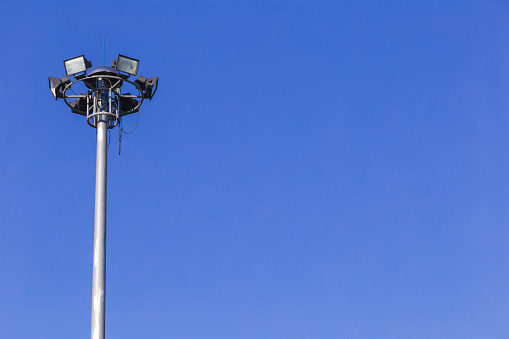 Spotlights tower high voltage in sport stadium on blue sky background.
