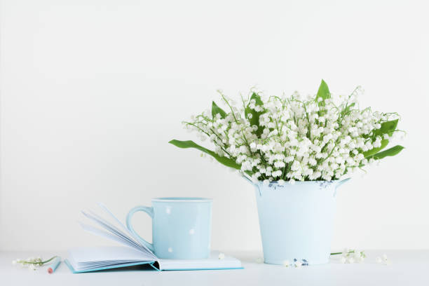 Lifestyle mockup decorated flowers in vase and coffee cup with notebook on white table with clean space for text and design.