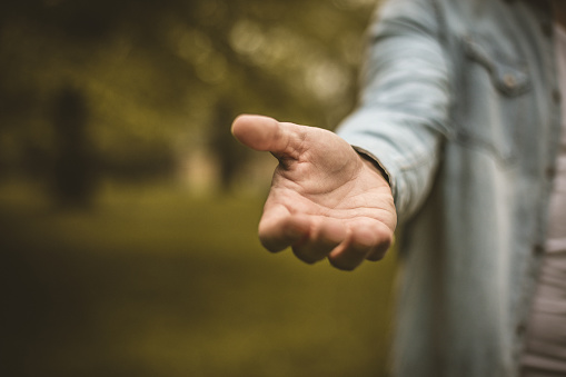 Young man in standing in park stretches his hand. Focus is on hand. Close up.