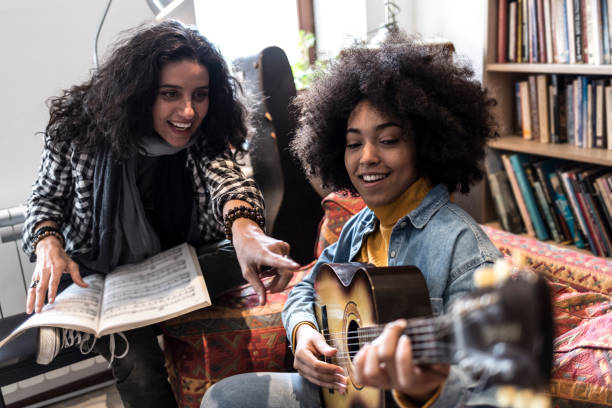 African woman learning playing a guitar with teacher, in studio.