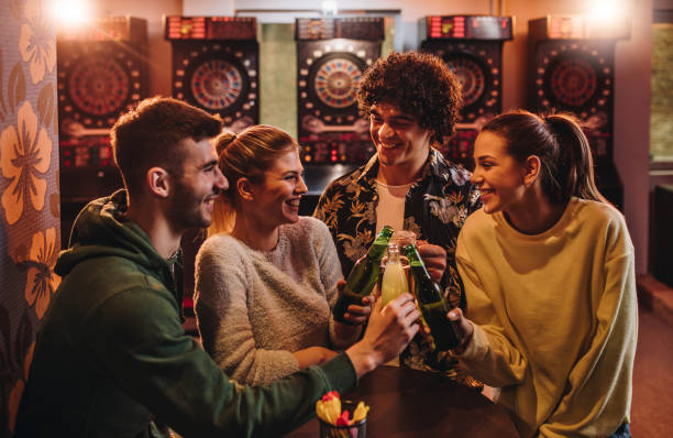 Young cheerful friends toasting after playing darts in a bar.
