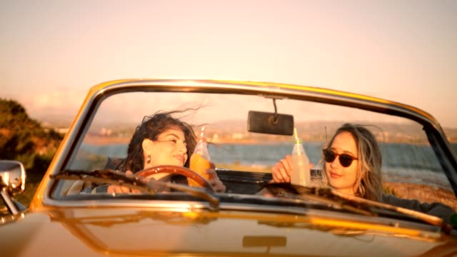 Women with soda relaxing in retro convertible car at beach