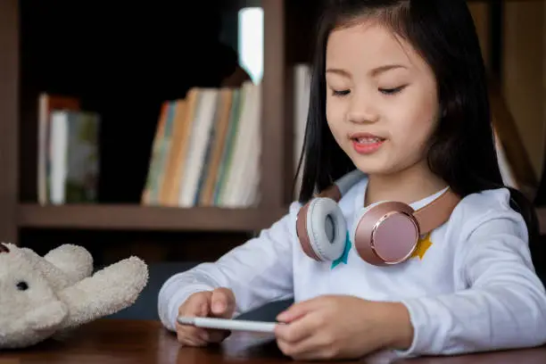 Photo of cute girl smile sitdown and playing tablet smartphone in the library, children concept, education concept