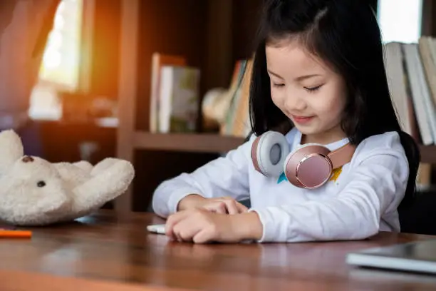 Photo of cute girl smile sitdown and playing tablet smartphone in the library, children concept, education concept