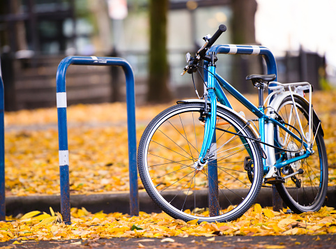 Amateur blue bicycle whose owner prefer an active healthy lifestyle is parked on the city street with autumn fallen yellow leaves  in the down town of the modern bicycle city of Portland