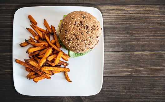 top view of plate with burger and sweet potato fries on rustic wooden table