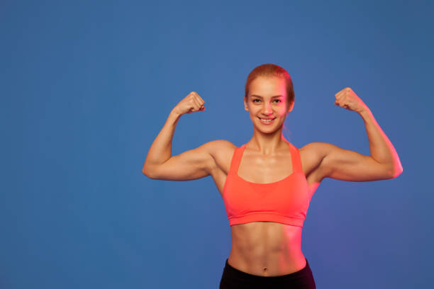 istock blond female athlete showing biceps on blue background, 959836534