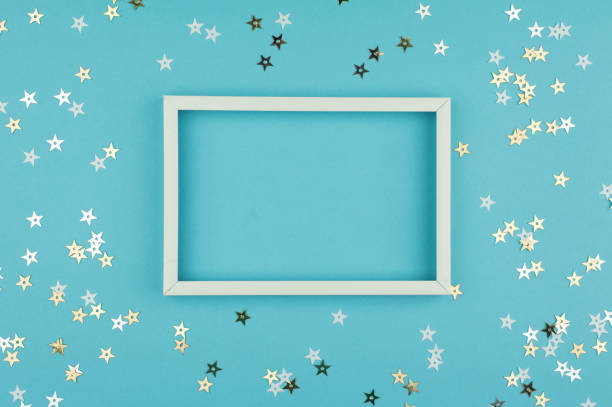 istock White picture frame and sequins stars on blue background. Top view, flat lay. Mockup for party or birthday invitation. 959844008