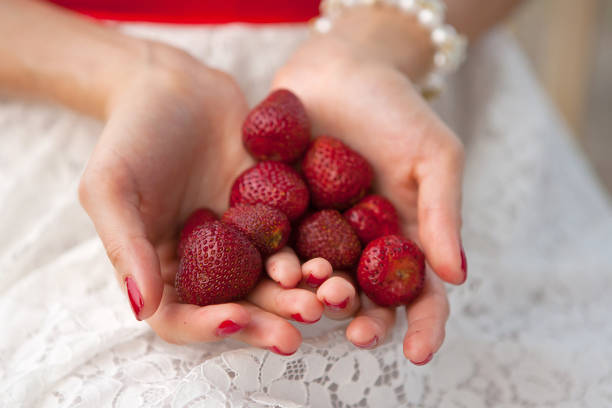 Female hands hold a handful of red strawberries without leaves. Picking berries in the summer, demonstrating the harvest. Healthy food, vegetarianism, small portions, natural raw foods. View from above. Side view.