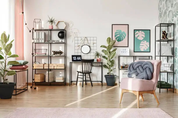 Sun beams illuminating modern home office in a trendy living room interior with industrial box frame furniture with pink elements