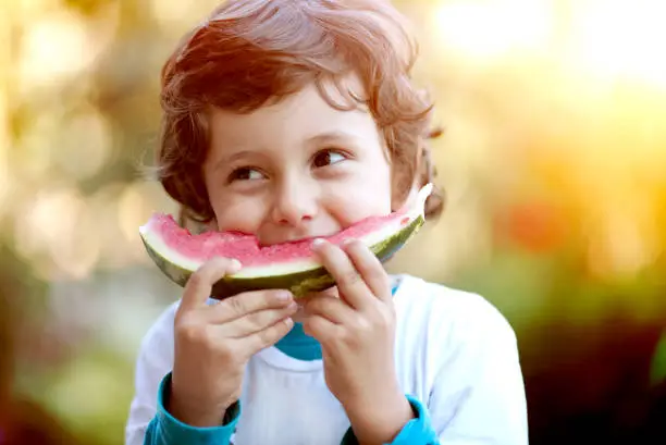 Photo of Cute boy child eating healthy organic watermelon in garden, nature background, sunny lights