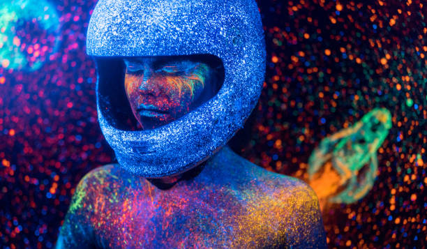 Beautiful teenage girl is posing on luminous starry sky  background with rocket. Eccentric fluorescent (neon, luminescent) painting on a face (the makeup) and on a body (the body art). Studio shooting in ultraviolet lighting