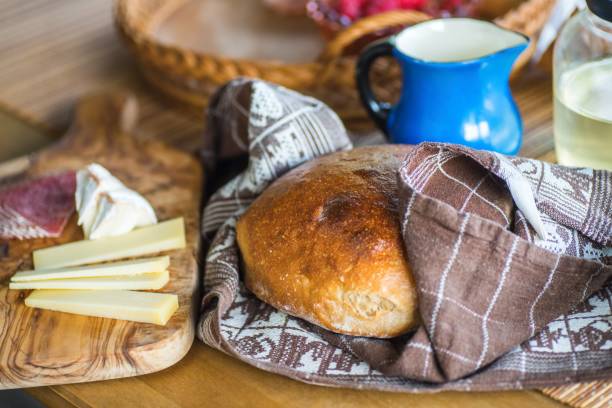 Bread in towel, blue pitcher, salami and cheese.