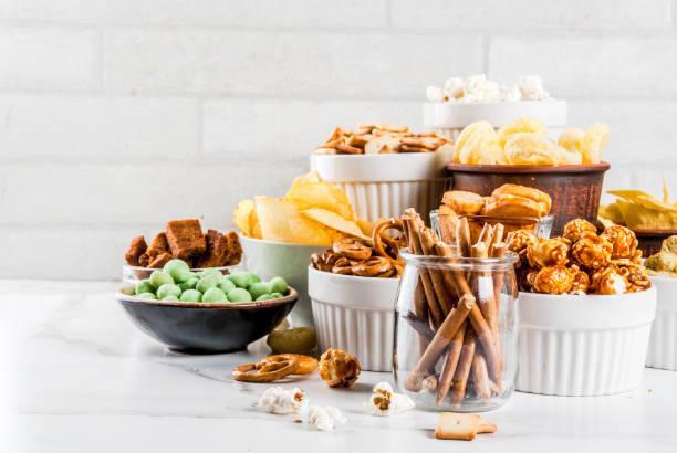 Variation unhealthy snacks Variation different unhealthy snacks crackers, sweet salted popcorn, tortillas, nuts, straws, bretsels, white marble background copy space savory stock pictures, royalty-free photos & images