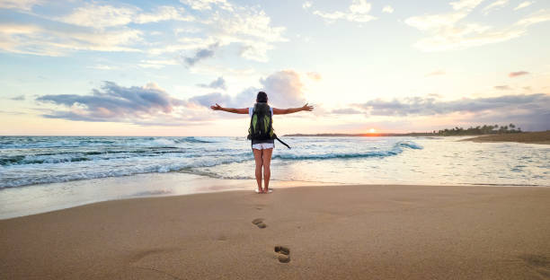 istock Woman backpacker greeting a sunset at the ocean coast 959889740