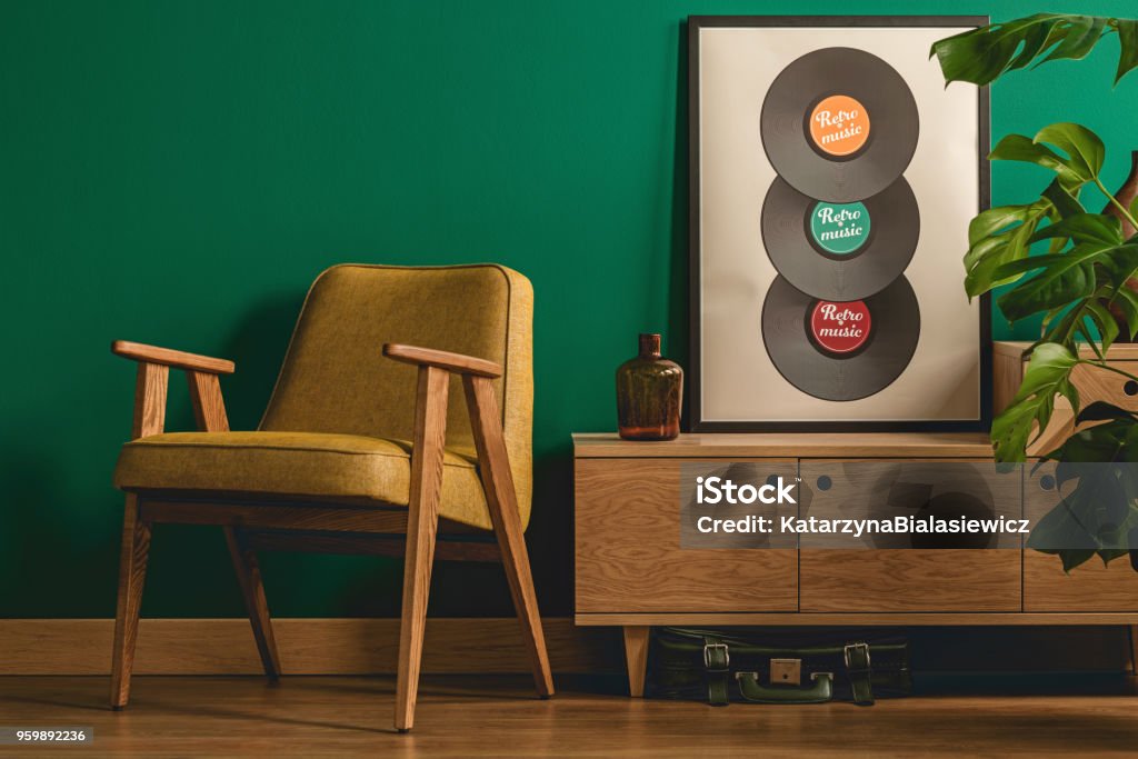 Armchair next to cabinet Retro armchair standing next to a wooden cabinet with a poster on top set on the dark green wall Music Stock Photo