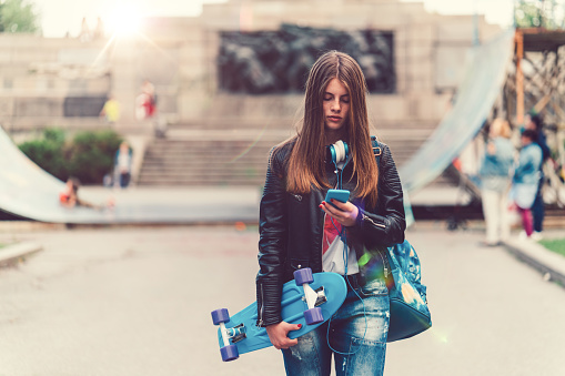 Young woman with skateboard texting on phone while walking